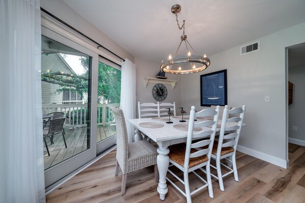 A dining area with a white table and chairs, a chandelier, and a view of a deck through a sliding glass door.
