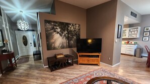 Un salón con televisor de pantalla plana, mueble de madera para entretenimiento, alfombra estampada y un cuadro abstracto grande en la pared.