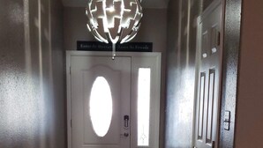Een hal met een bank, een deur met een rond raam en een plafondlamp.