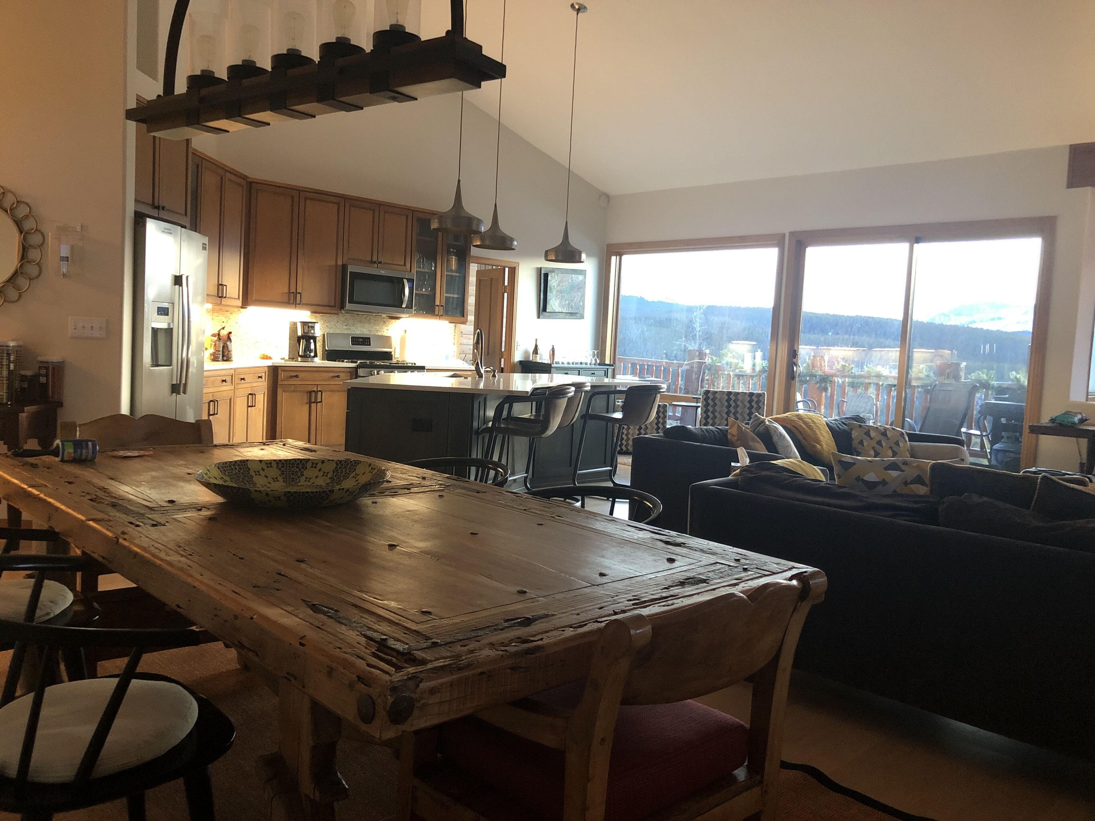 Amplia sala de estar con una mesa de comedor de madera, un sofá y vistas a un paisaje montañoso a través de grandes ventanales.