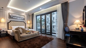 A modern hotel room with a large bed, a sofa, a desk, and a balcony with a view of buildings. - Babylon Premium Hotel & Spa (Hanoi)