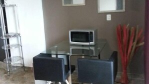 Un saló modern amb una taula de vidre, dues cadires negres, un televisor de pantalla plana, un microones i un vas decoratiu.