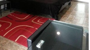 Un dormitori amb un llit gran, una taula petita, un feser vermell i una finestra.