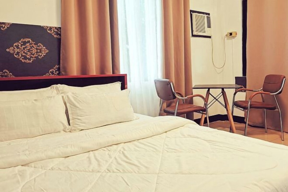 A hotel room with a bed, two chairs, a small table, and a mirror.