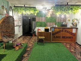 Una zona de recepción con un mostrador de madera, un perro acostado en el suelo y plantas artificiales.
