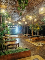 Un jardín interior con bancos de madera, luces colgantes y abundante vegetación.