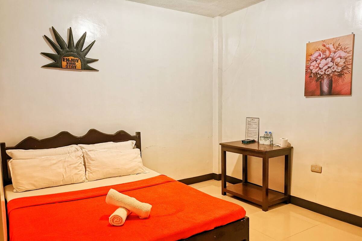 A hotel room with a bed, a small table with toiletries, a wall decoration, and a painting.