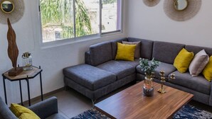 Un saló modern amb un sofà seccional gris, una taula de centre de fusta i una taula auxiliar amb elements decoratius.