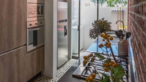 Una cuina moderna amb electrodomèstics integrats, una porta de vidre que dona a un balcó i una planta decorativa.