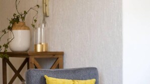 Una cadira grisa amb un coixí groc en una habitació que té una taula consola de fusta i un ram amb plantes verdes.