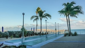 A beachfront walkway with palm trees, a pool, and a pier in the background. - Oceanview Condo 2bed/2bath beachfront condo in Key Colony Beach (Key Colony Beach)