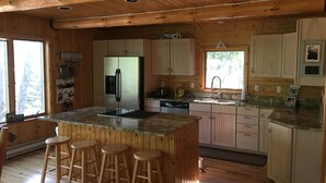 Interior de una cabaña de madera con cocina, que incluye un refrigerador, estufa, lavamanos y taburetes de bar.