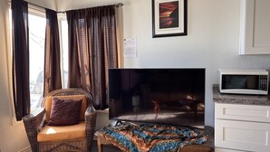 A living room with a television, a microwave, and a wicker chair with cushions. - Ocean-Front Beach Bungalow with Two Bedrooms and a shared Ocean-Front deck (San Clemente)