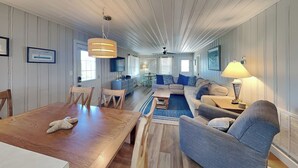 Un salón amplio con una mesa de comedor de madera, sofás azules y un ventilador de techo.