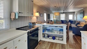 Una cocina compacta con armarios blancos, horno empotrado e isla central con estantes para almacenamiento.