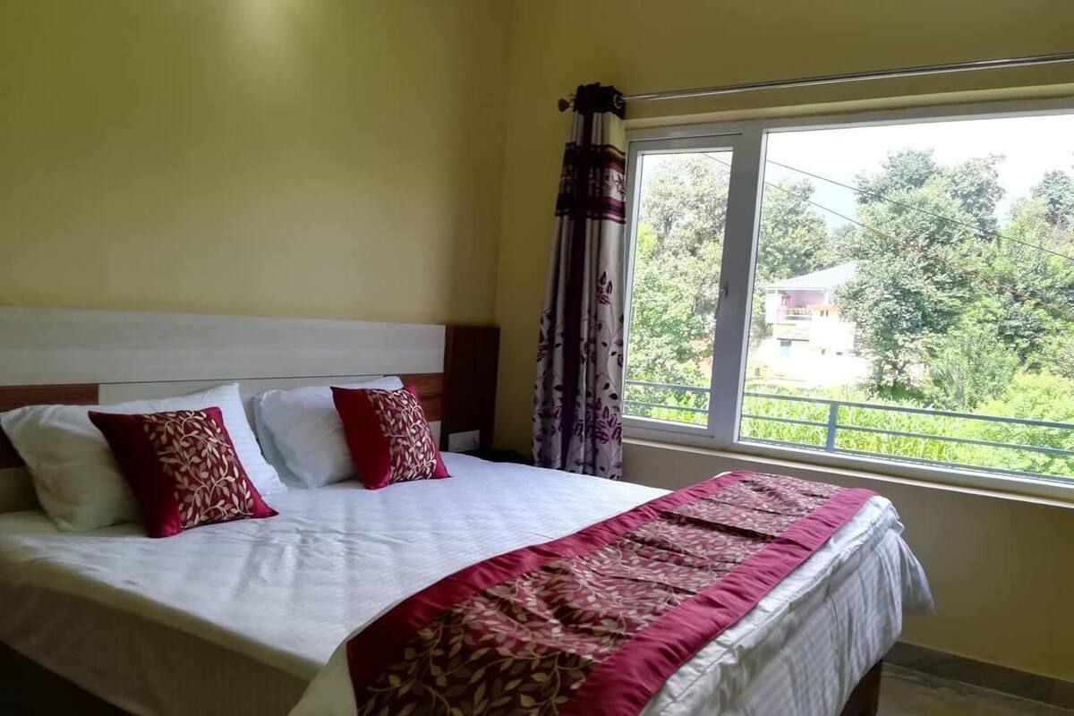 A neatly made bed with white and red bedding, a headboard, and a window with a view of greenery outside.