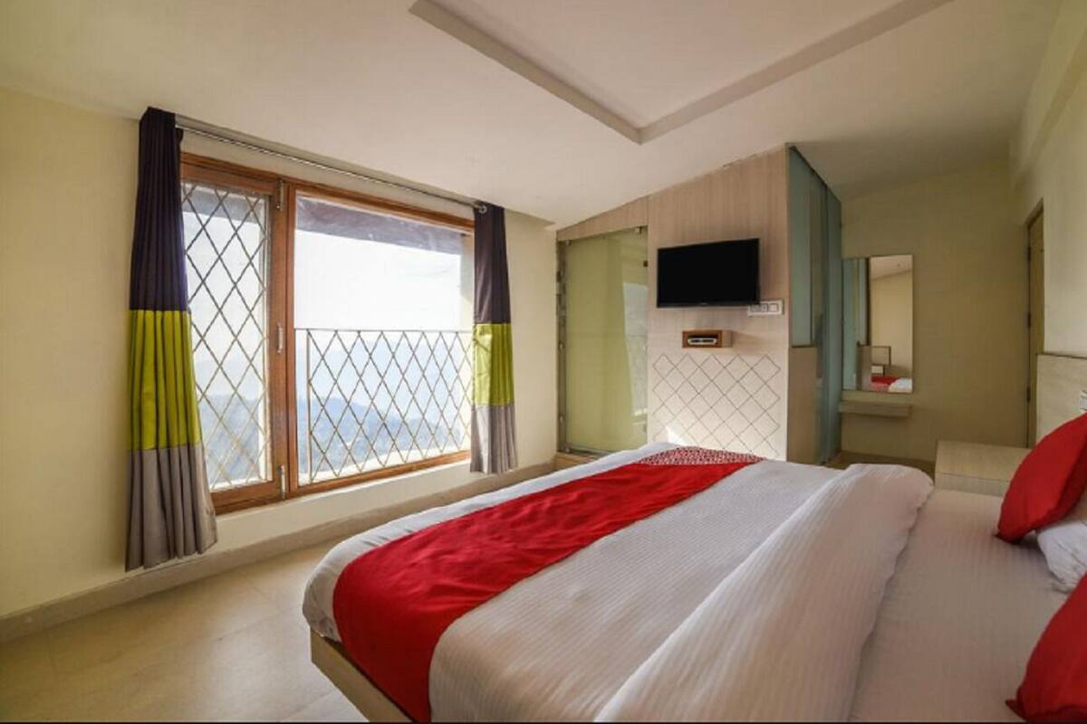 A hotel room with a large bed, a TV mounted on the wall, and a window with curtains.