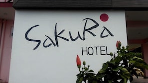 A sign for Sakura Hotel with the name in stylized text and a red dot. - Sakura Guest House (Dharamshala)