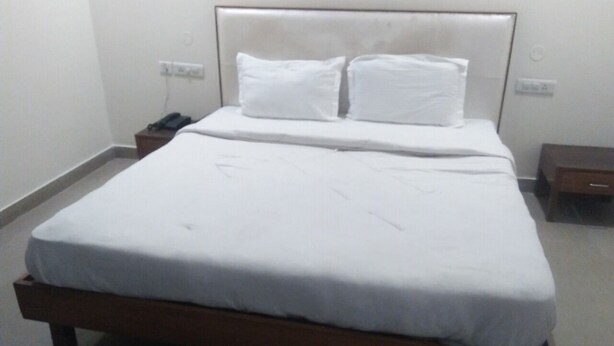 Una cama bien hecha con sábanas y almohadas blancas, una mesita de noche con un teléfono y un enchufe de pared.