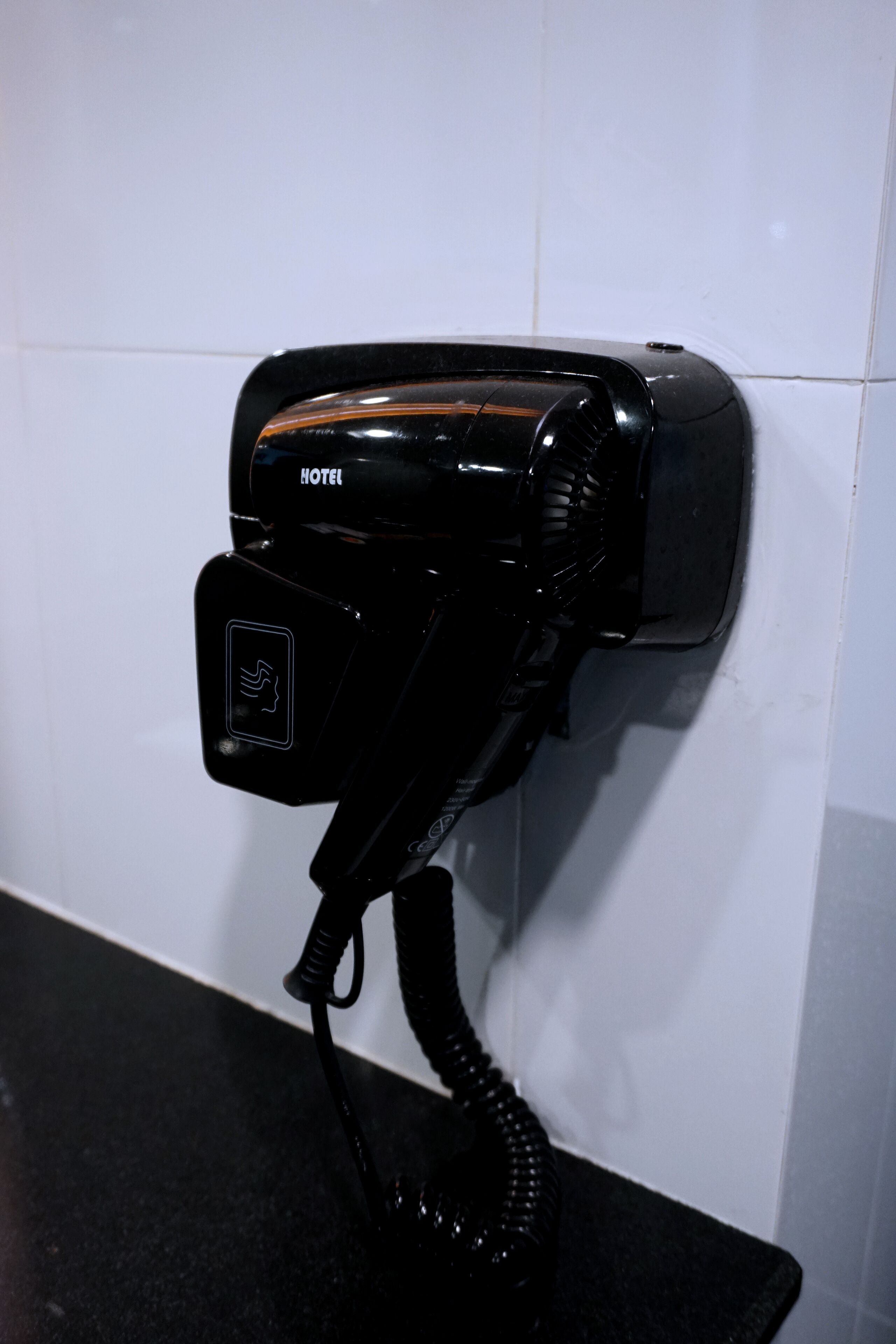 A black hair dryer mounted on a white tiled wall.