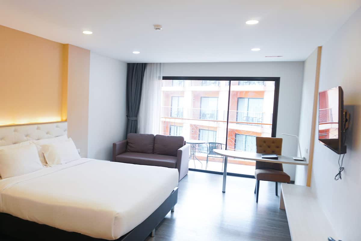 Quarto de hotel com uma cama grande, um sofá, uma escrivaninha e uma televisão.