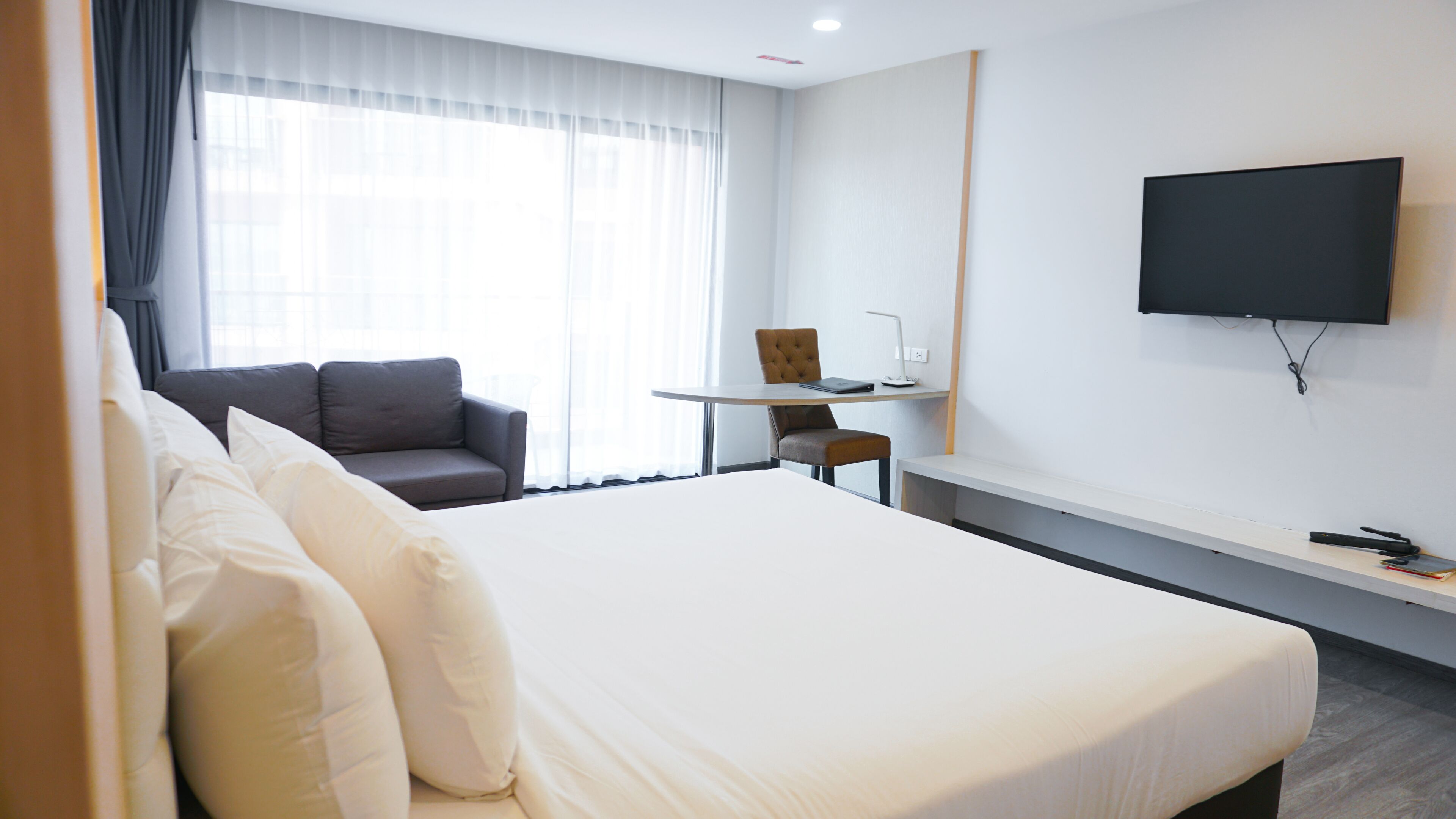 Ein Hotelzimmer mit einem großen Bett, einer Couch, einem kleinen Tisch und einem an der Wand befestigten Fernseher.