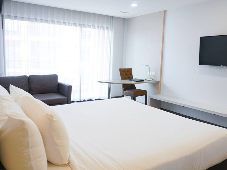 Ein Hotelzimmer mit einem großen Bett, einer Couch, einem kleinen Tisch und einem an der Wand befestigten Fernseher.
