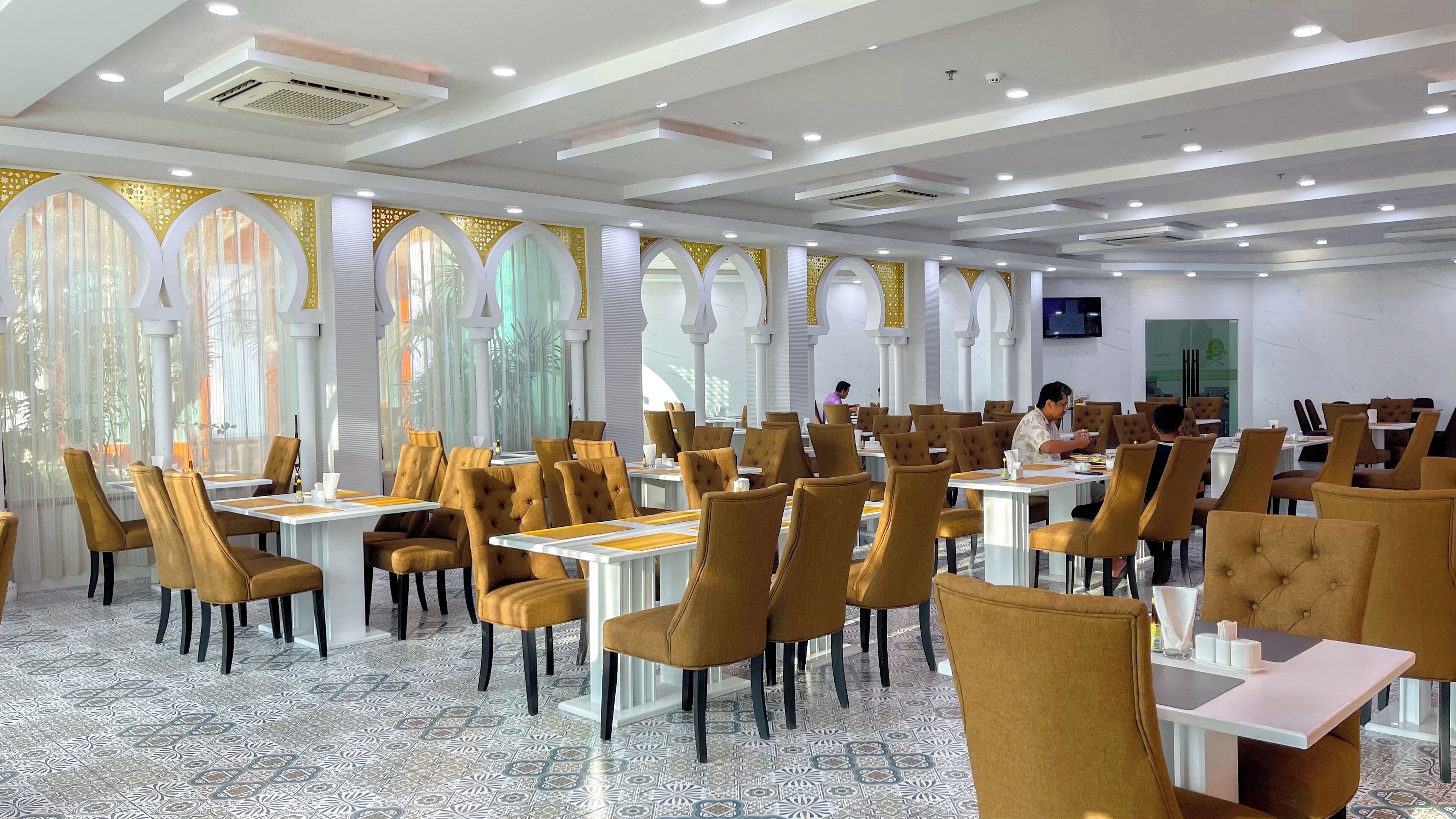 Un comedor espacioso con mesas y sillas altas, ventanas grandes con diseños decorativos y un diseño de techo moderno.