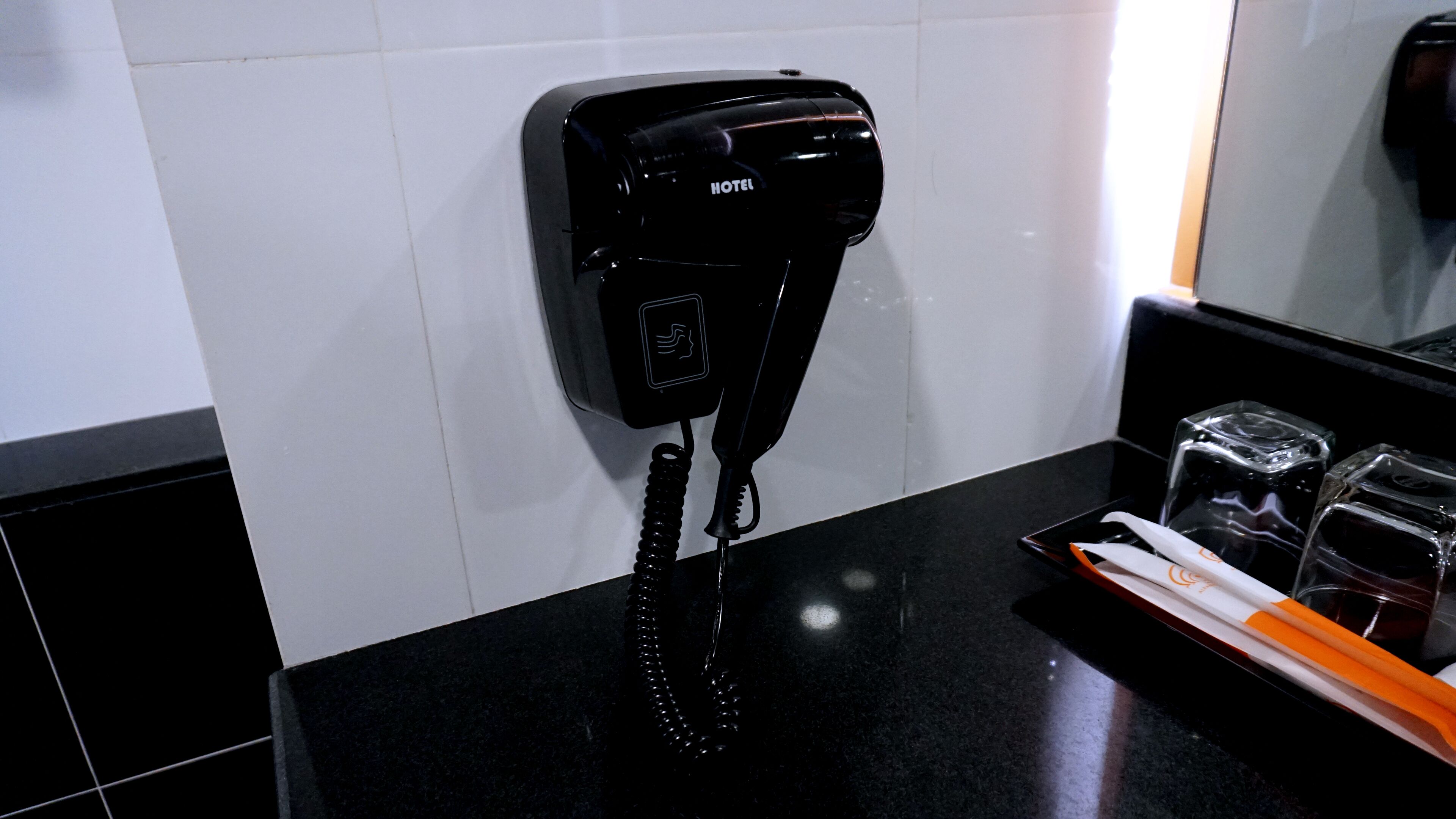 Teléfono de hotel negro con cable enrollado, un espejo y una bandeja con vasos y una botella.