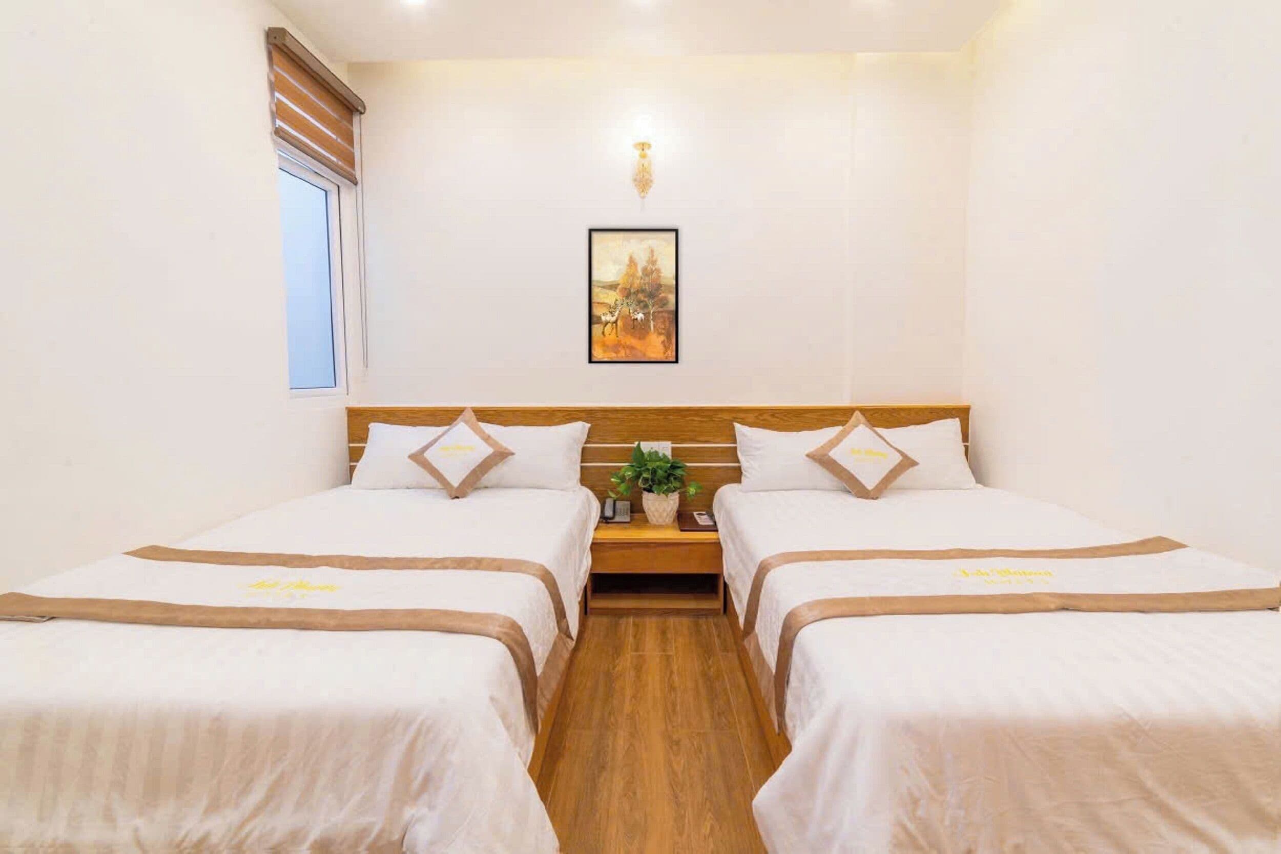 A hotel room with two beds, a nightstand, a wall-mounted light, and a window with blinds.