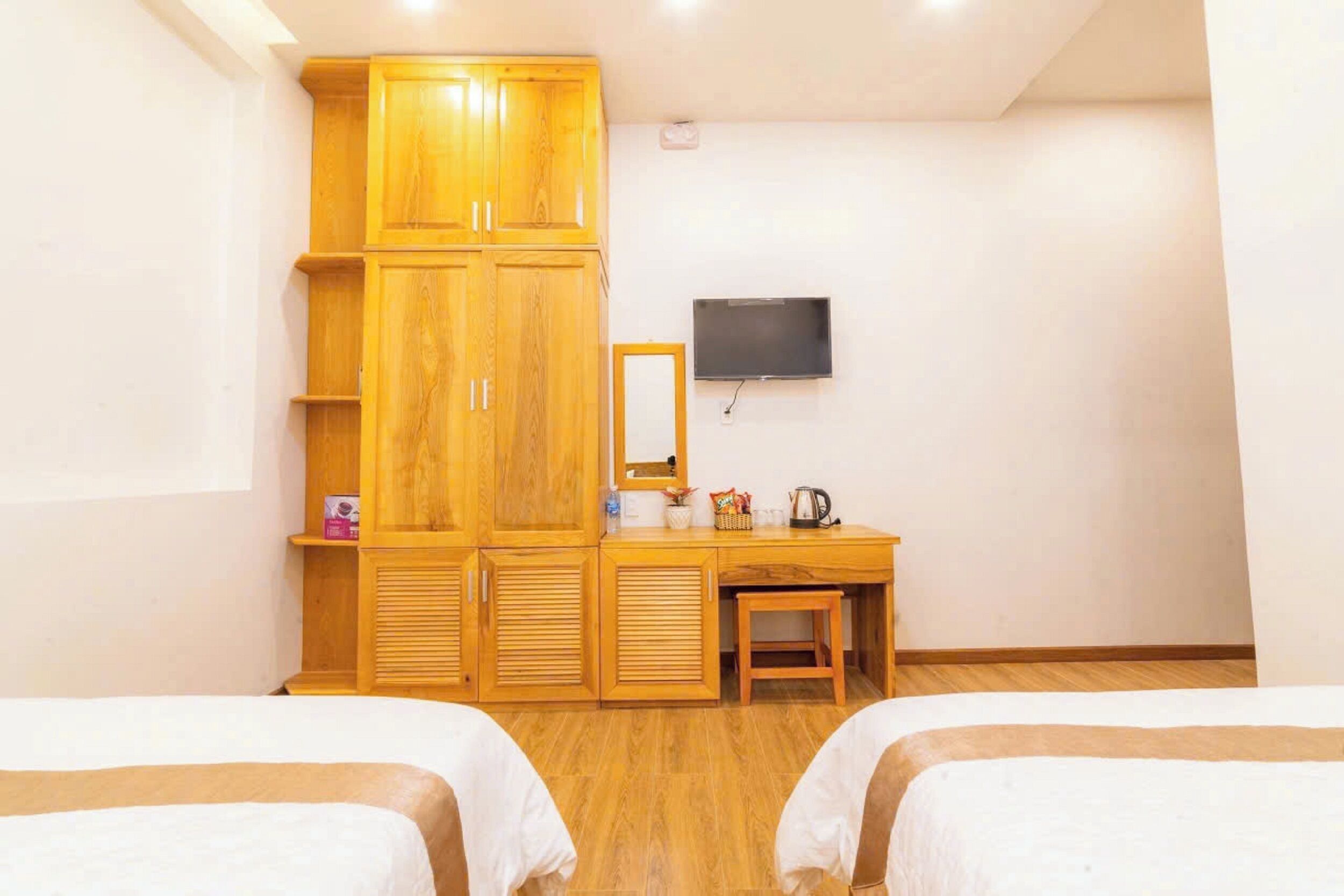 Een hotelkamer met twee bedden, een houten garderobe, een bureau met spiegel en een wandgemonteerde flatscreen televisie.