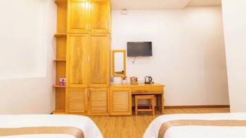 Een hotelkamer met twee bedden, een houten garderobe, een bureau met spiegel en een wandgemonteerde flatscreen televisie.