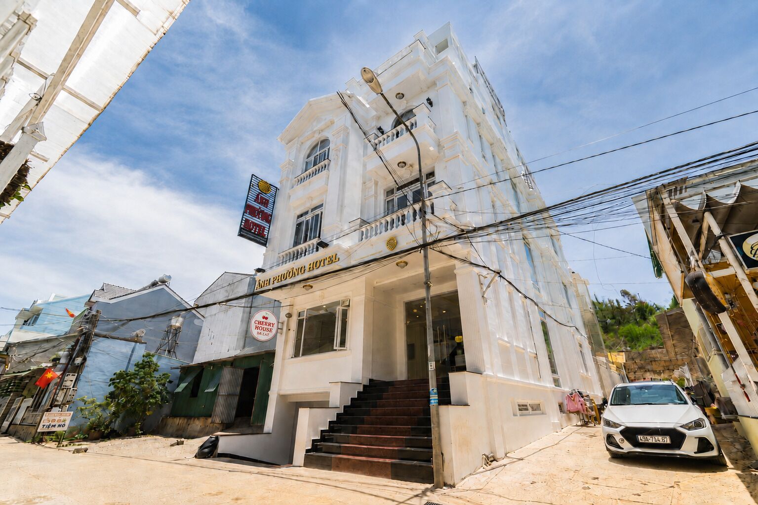 A hotel with a prominent sign, a staircase leading to the entrance, and a parked car in front.