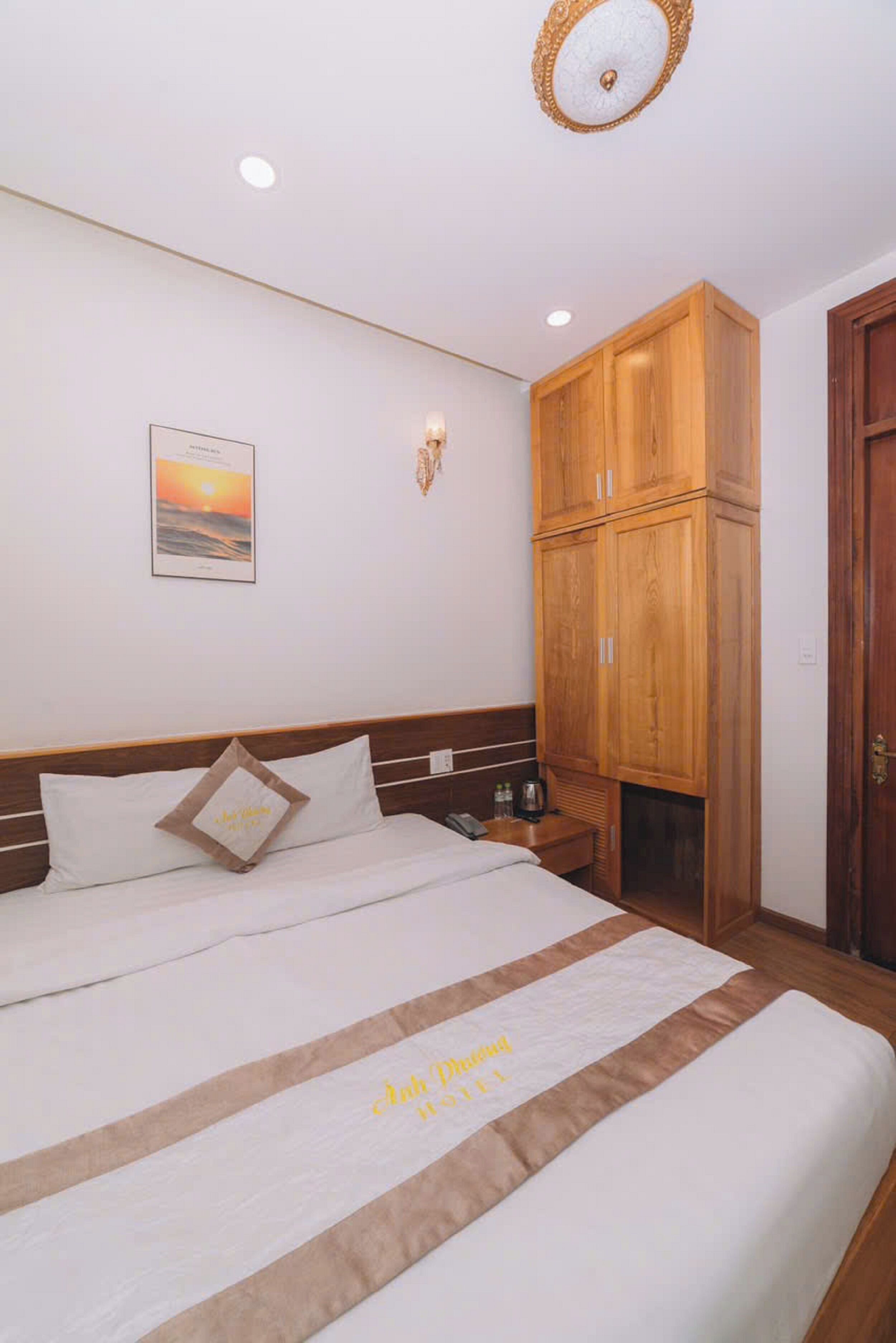 A hotel room with a bed, a nightstand, a wooden wardrobe, and a wall-mounted light fixture.