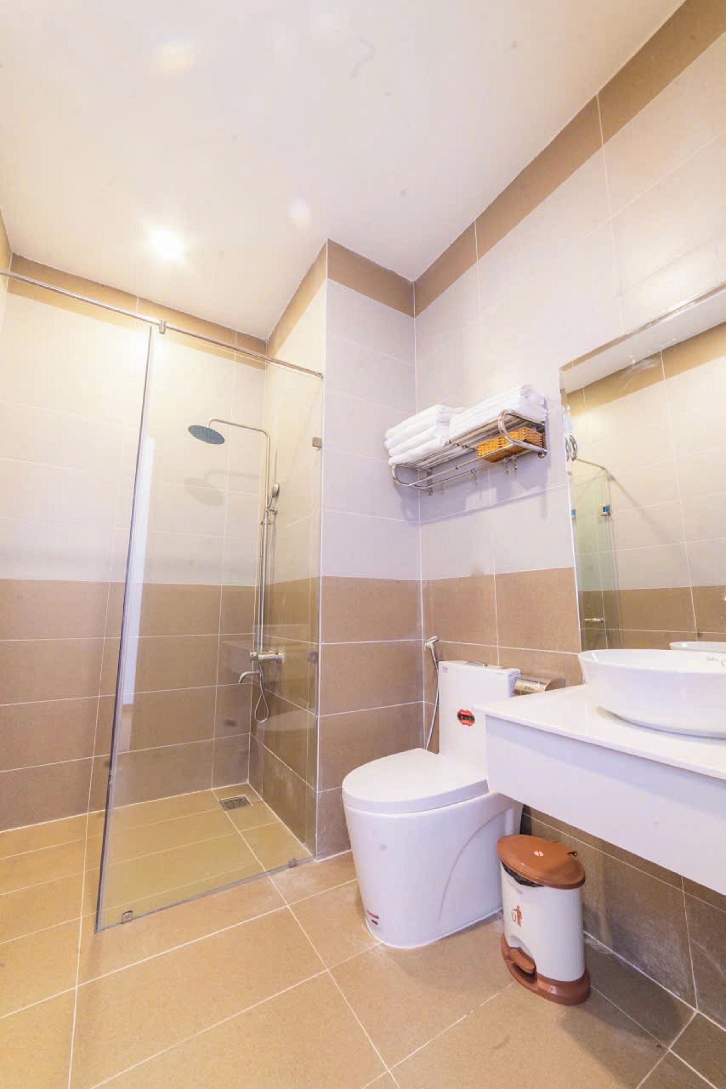 A modern bathroom with a glass-enclosed shower, a toilet, and a sink with a towel rack above.
