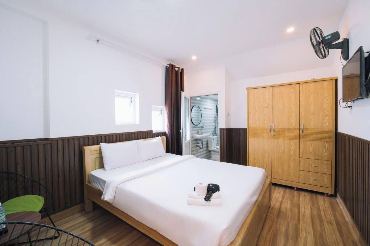 A hotel room with a wooden bed, a wardrobe, a TV, and a bathroom visible through an open door.