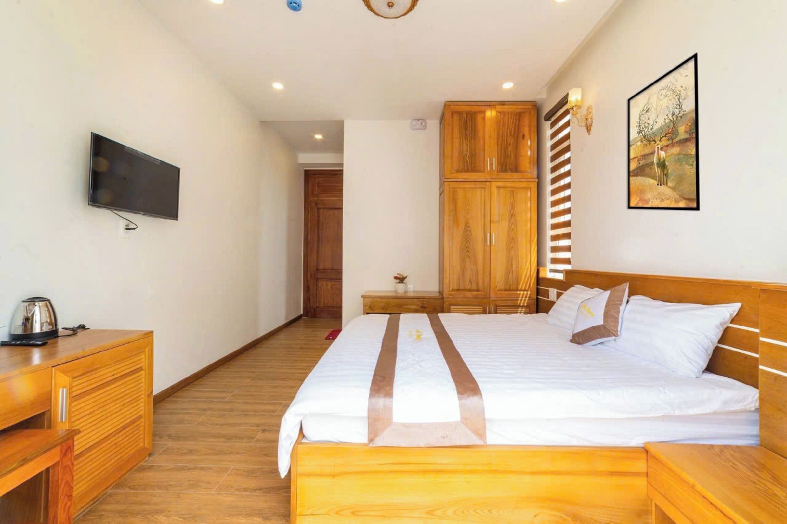 A hotel room with a bed, wooden wardrobe, a television, and a painting on the wall.