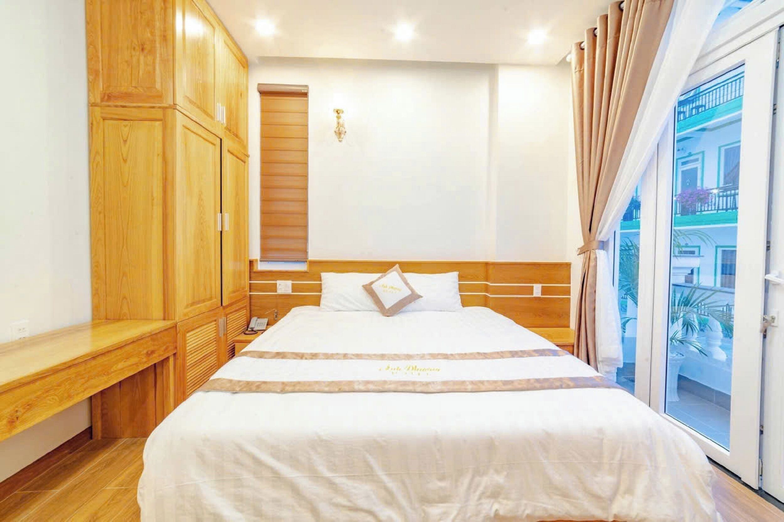A hotel room with a bed, wooden wardrobe, and a view of the outside.