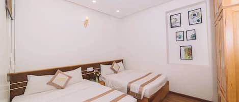 A hotel room with two beds, a wooden wardrobe, and a wall with framed pictures.
