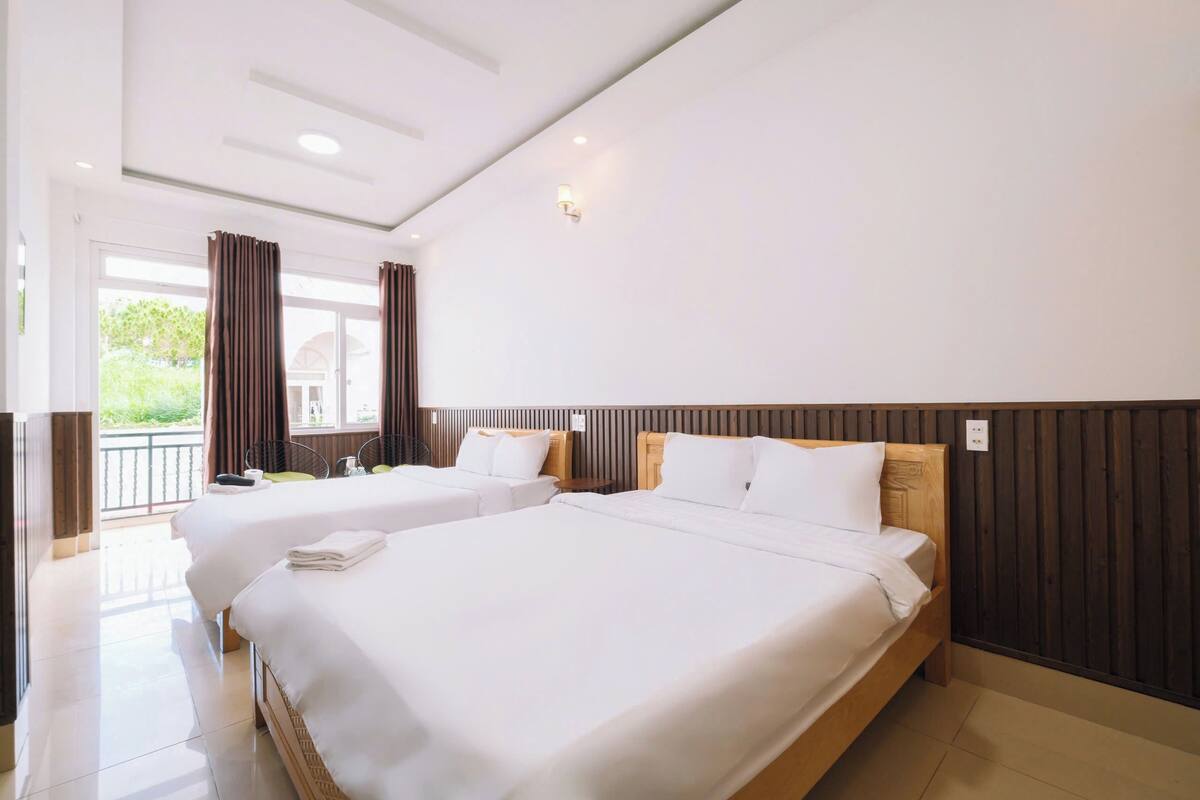 A hotel room with two beds, a wooden headboard, a large window with curtains, and a balcony.