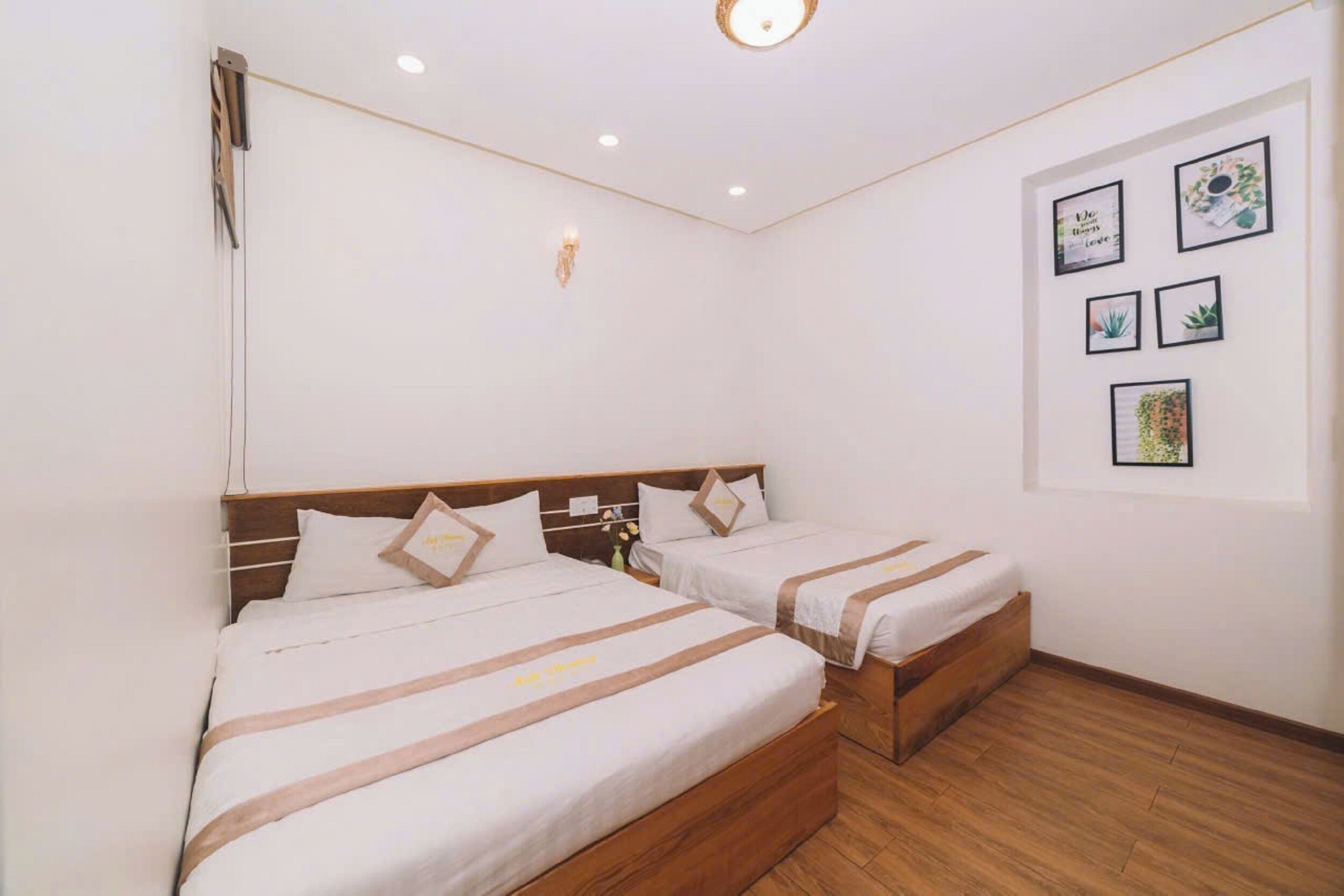 A hotel room with two beds, a wooden floor, and a wall with framed pictures.
