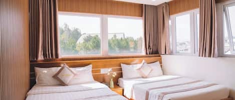 Habitación de hotel con dos camas, cabecera de madera, mesita de noche y ventana con cortinas.