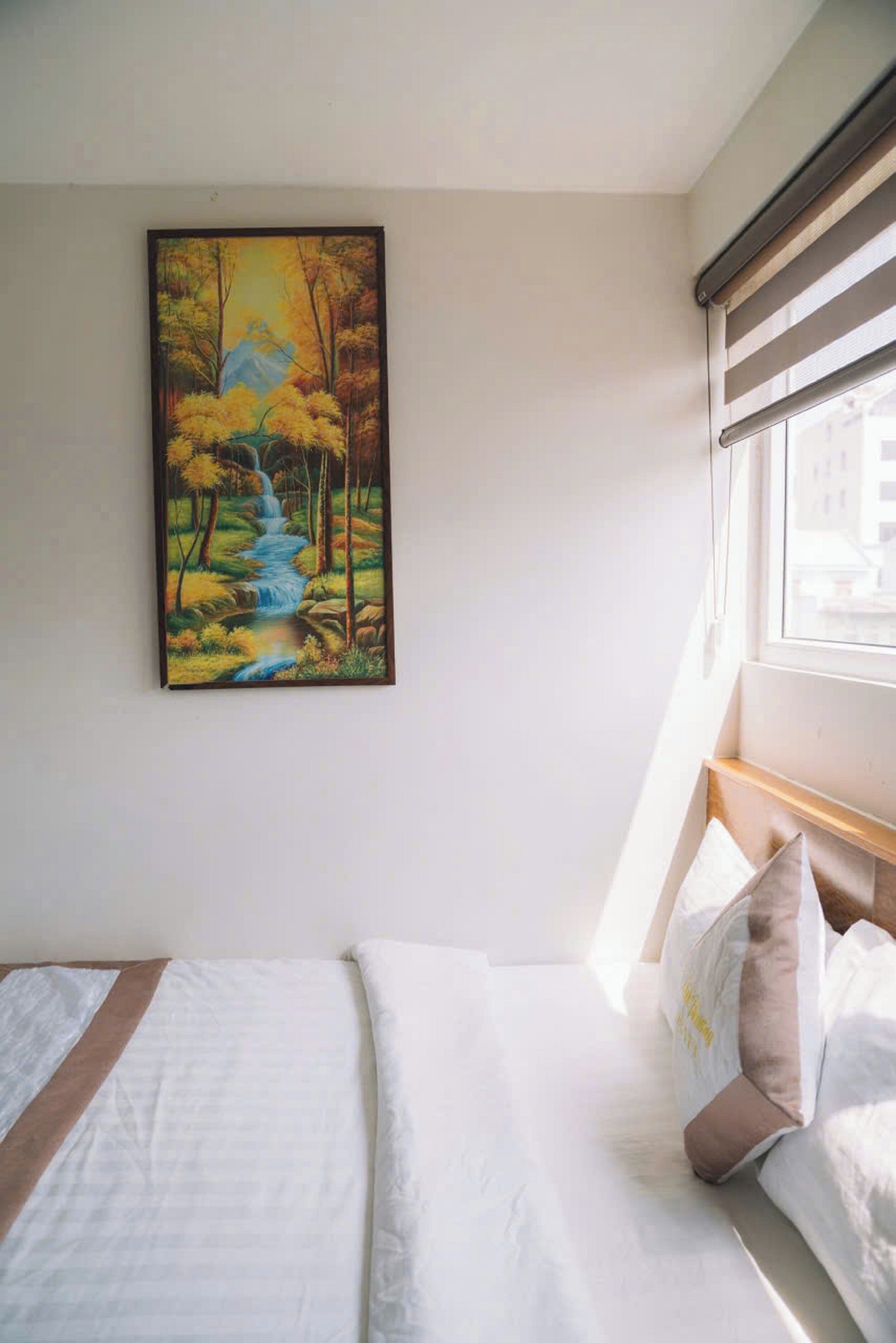 Quarto de hotel com uma cama, um quadro de um riacho em meio à floresta e uma janela com persianas.