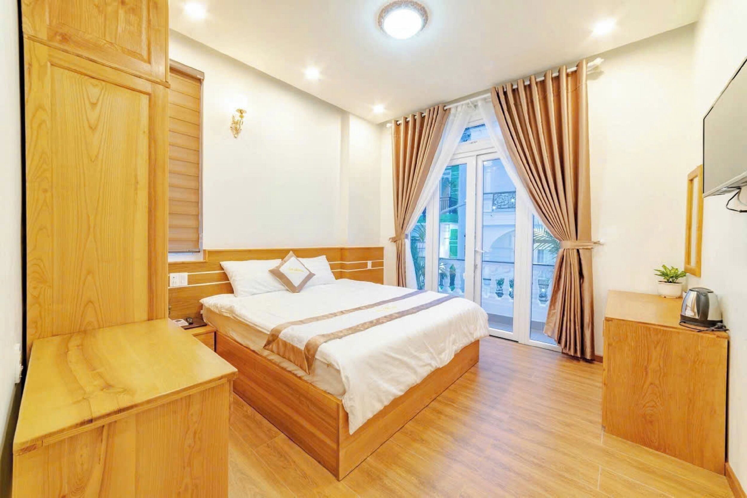 A hotel room with a wooden bed, a bedside table, a small cabinet, a window with curtains, and a view of the outside.
