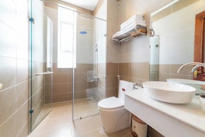 Un baño moderno con cabina de ducha de vidrio, un lavabo blanco y un inodoro.