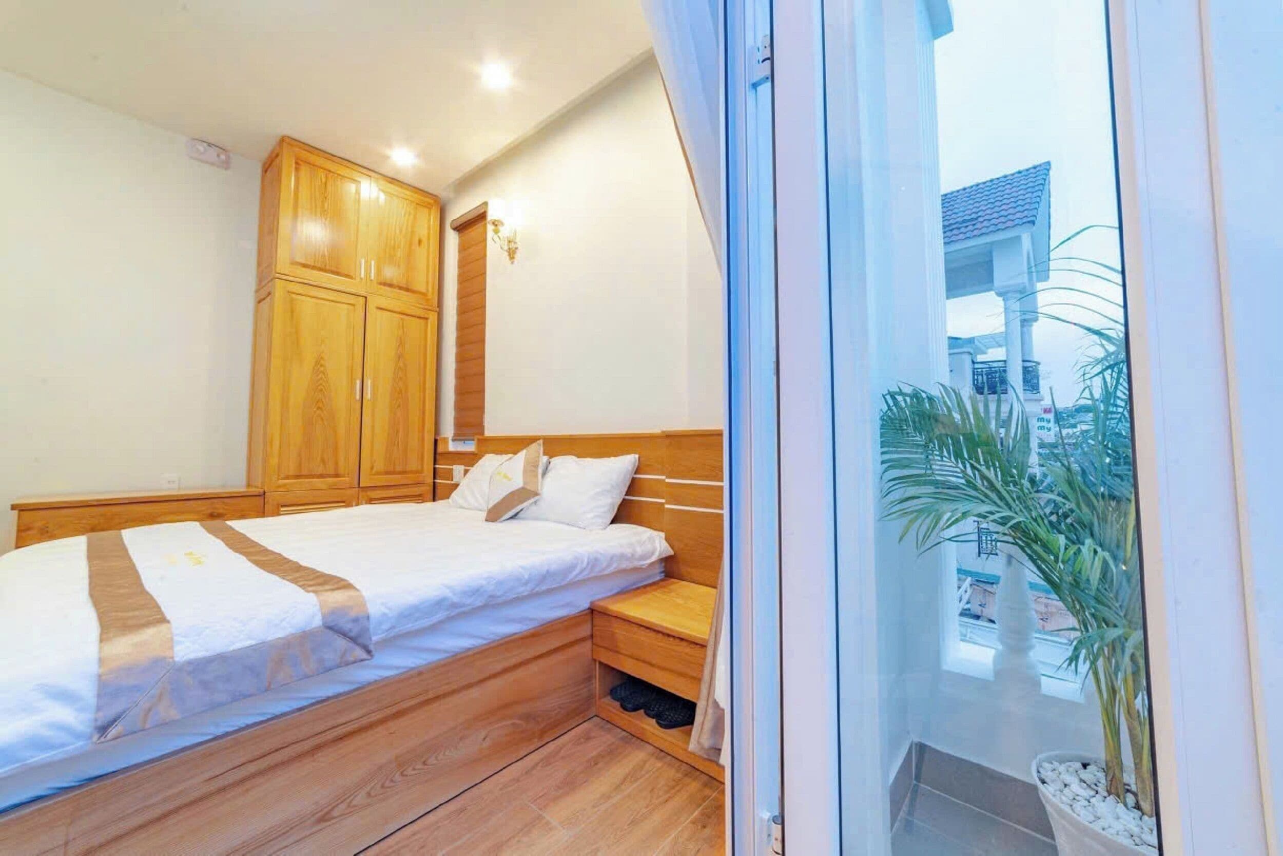 Un dormitorio con una cama de madera, una mesita de noche, un armario y vistas a palmeras a través de una ventana.
