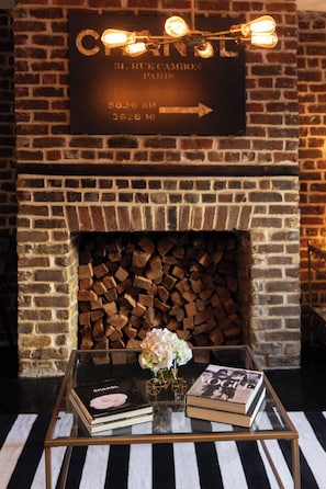 A brick fireplace with a sign above it, a glass coffee table with books and a vase, and a striped rug on the floor.