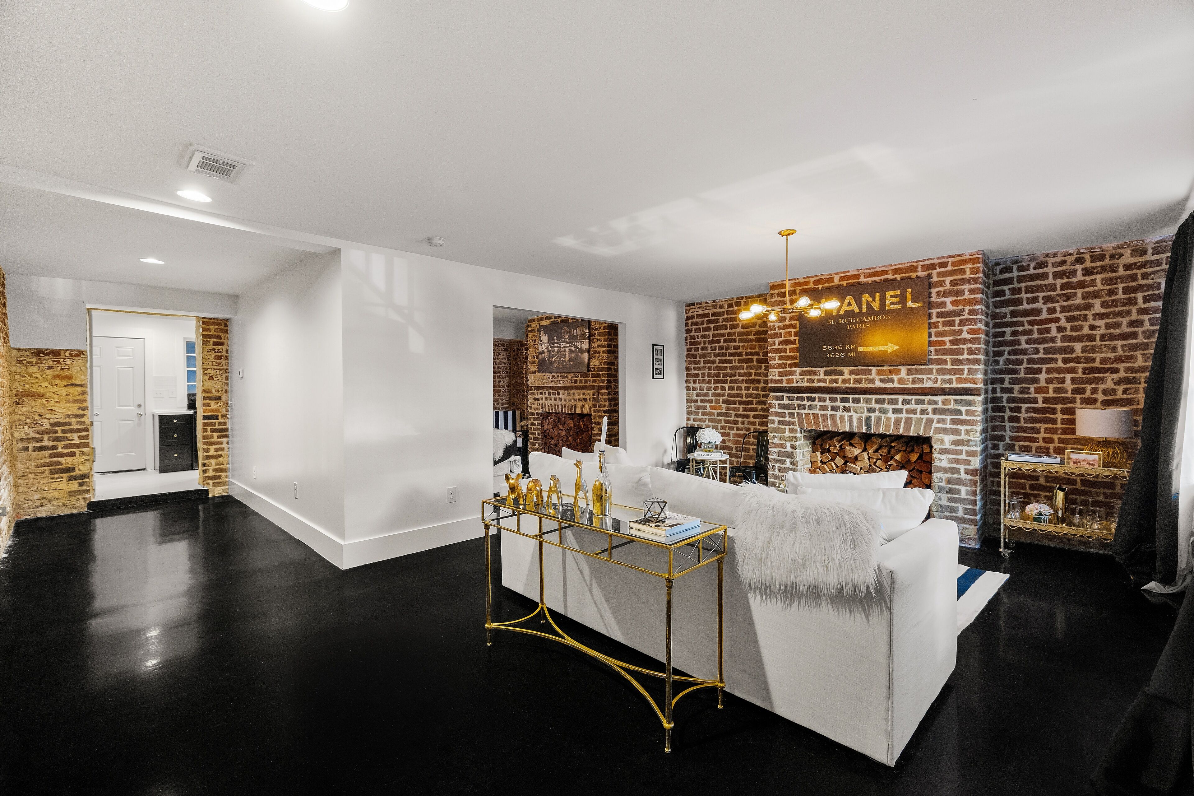 A modern living room with a white sofa, a glass coffee table, and a brick fireplace.