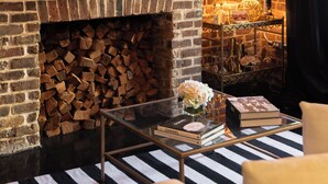 A brick fireplace with a sign above it, a glass coffee table with books and a vase, and a chandelier. - Luxury Townhouse Chic Flat in the Historic Center! (savannah)