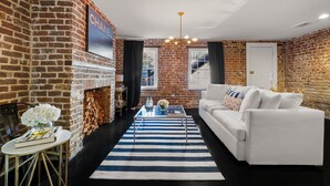 A modern living room with a white sofa, a striped rug, and a brick wall. - Luxury Townhouse Chic Flat in the Historic Center! (savannah)